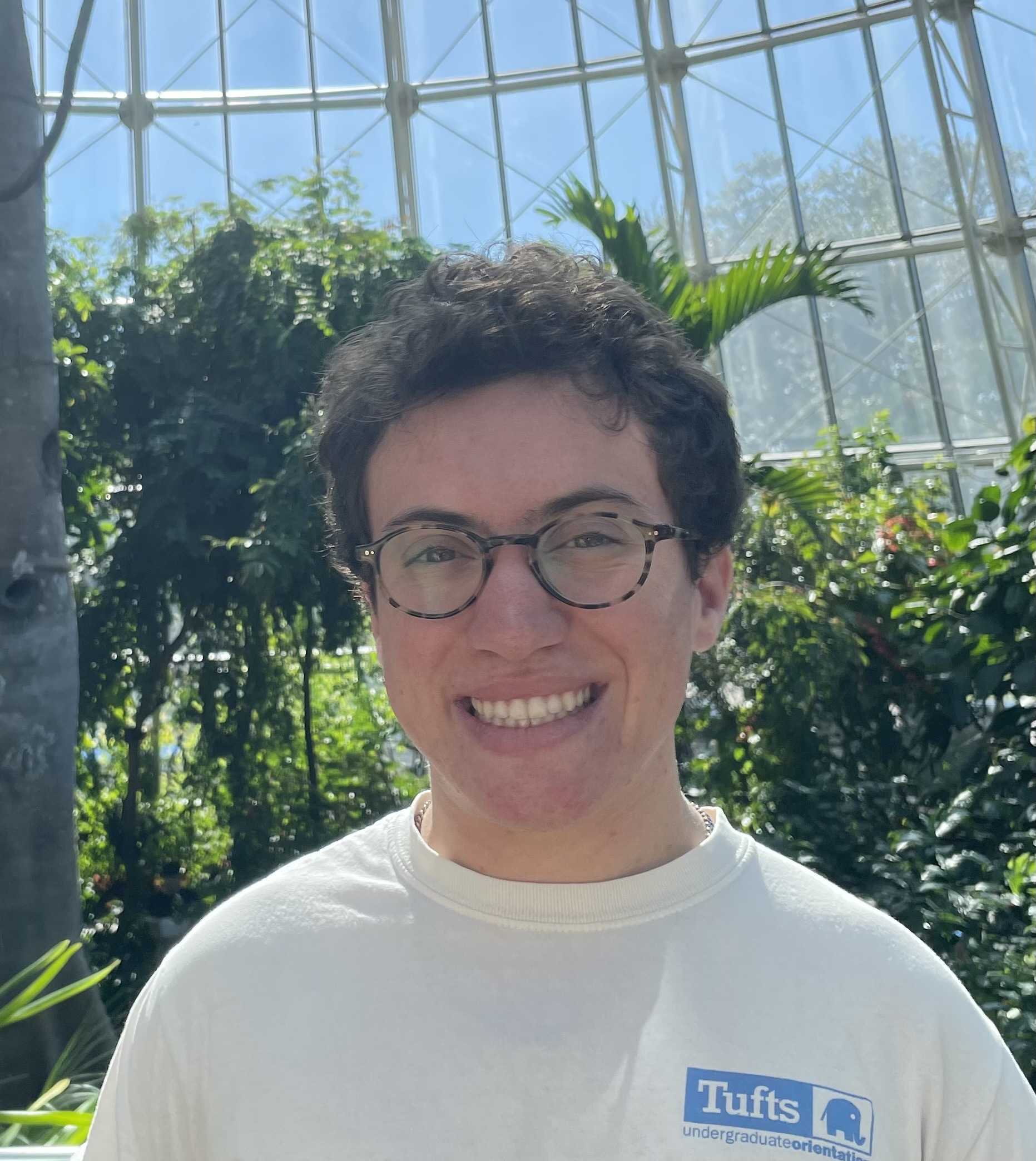 A photo of me, a white man, smiling. I am wearing glasses and a Tufts t-shirt, and I have short, brown hair.